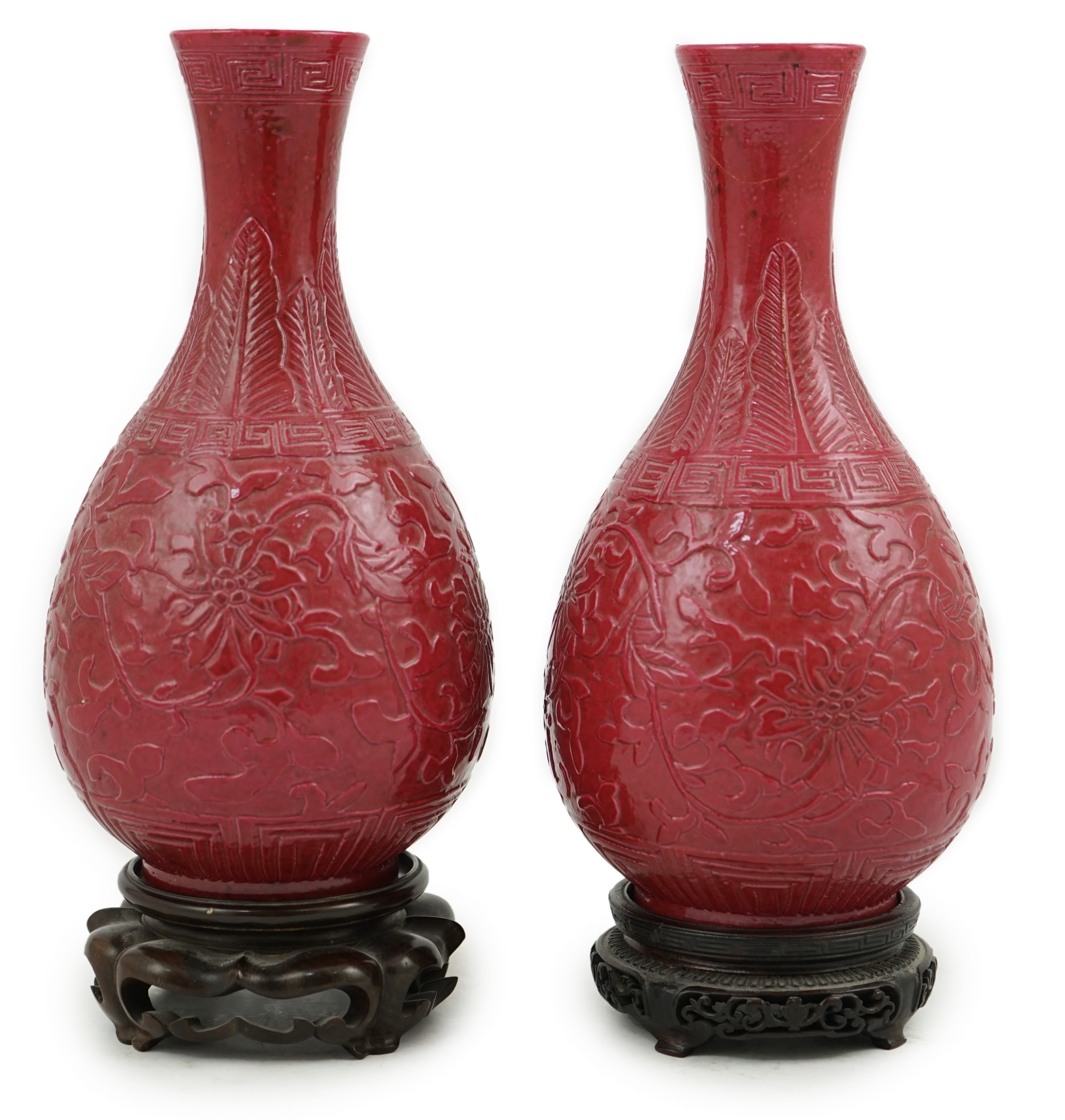 A pair of Chinese ruby ground ‘lotus’ bottle vases, late 19th century, each carved in relief with lotus flowers, scrolling tendrils and leaves, both with carved stands, 24cm high. Condition - one vase the neck broken bot